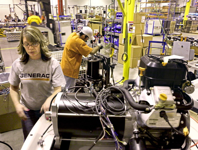 Tina Aukofer (foreground) works on a backup generator Monday at the Generac plant in Whitewater, while Adalberto Abreu (rear) connects an engine to a hoist to lift it into place on the assembly line. 
